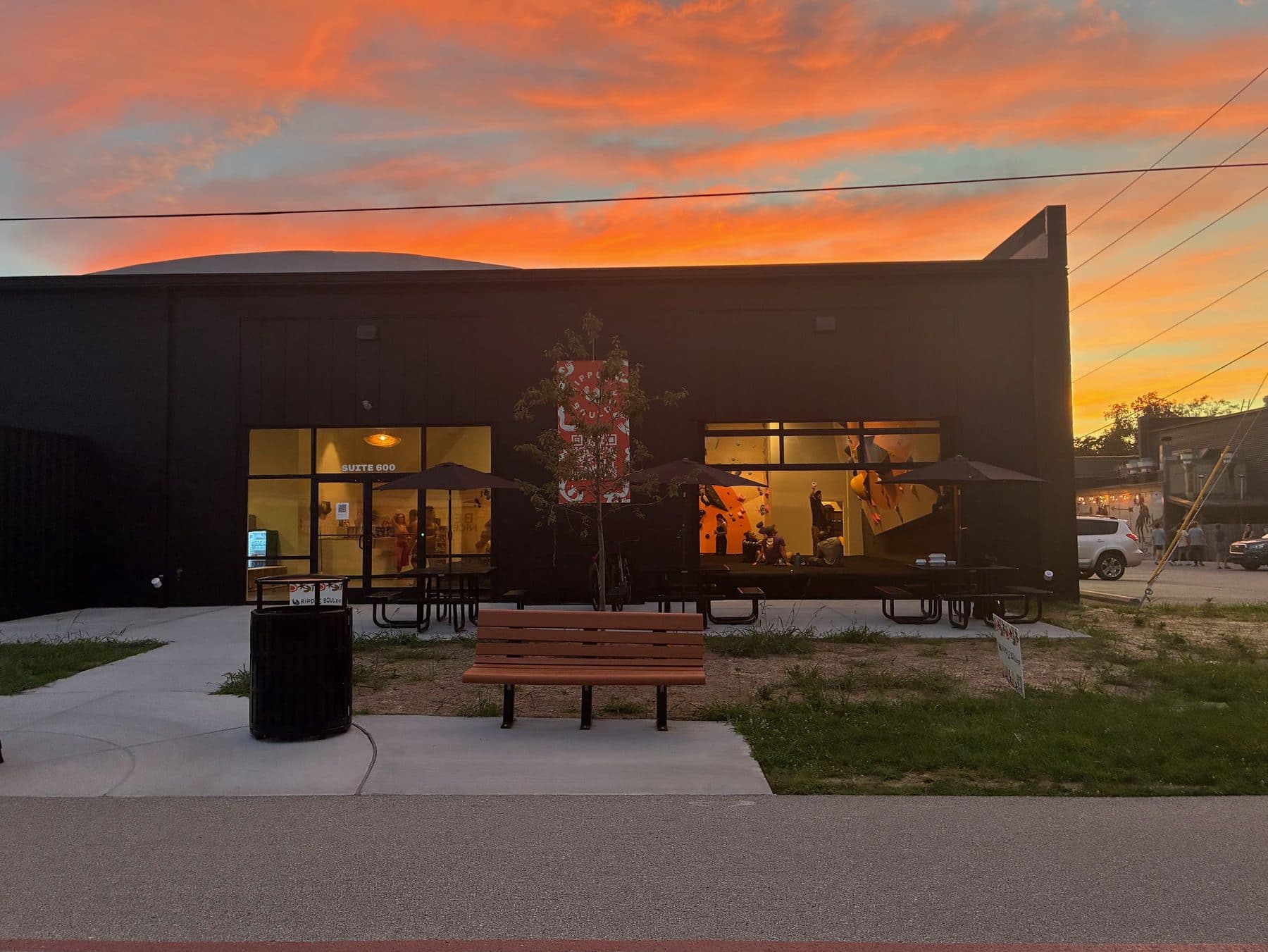Ripple Boulder’s black storefront at sunset — the patio tables out front and climbers visible through the lit windows